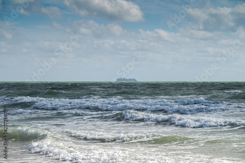 Ocean waves under a partly cloudy sky with a distant cruise ship on the horizon in Costa Ballena, Chipiona, Cádiz, Spain, capturing a coastal seascape with maritime travel and summer atmosphere.
