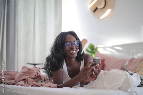 Quadro em tela Happy Black woman scrolling on her phone in bed