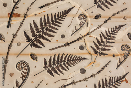 Seamless pattern featuring dark brown fossilized fern leaves, horsetail stems, and small stone textures on a light beige, weathered stone background