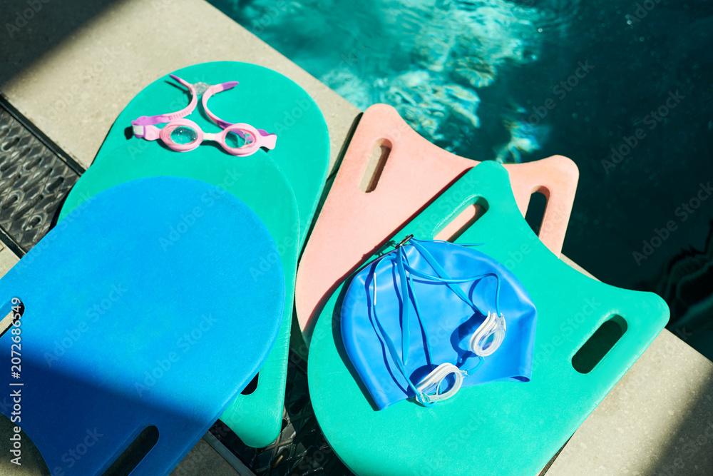 Naklejka premium Close up of childrens swimming lesson gear resting by pool, showing kickboards, goggles, swim cap for training and water safety. Useful for swim school, youth sports, fitness promotion