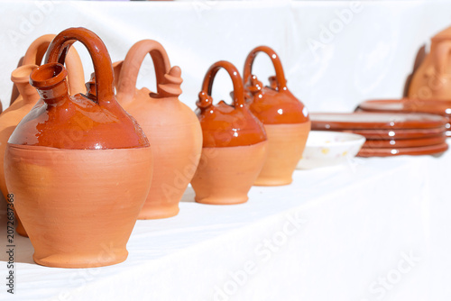 Traditional clay jugs and pottery displayed on a white surface at an outdoor artisan market.