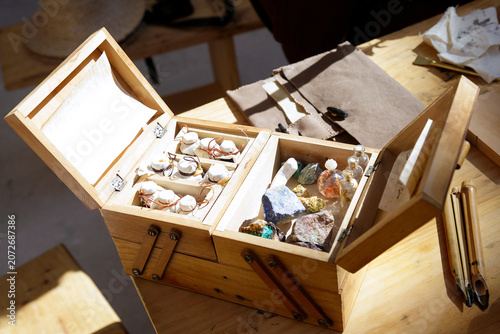 Handcrafted wooden box filled with minerals, small vials, and wrapped items arranged on a rustic workspace.