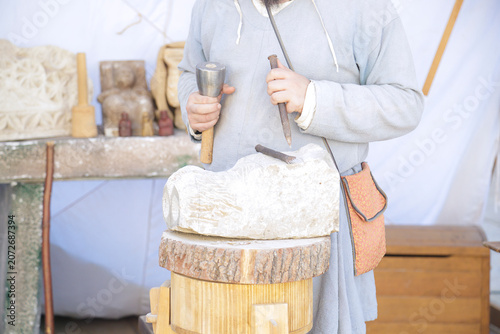 Artisan carving a decorative stone block with a hammer and chisel in a traditional stone‑carving workshop.