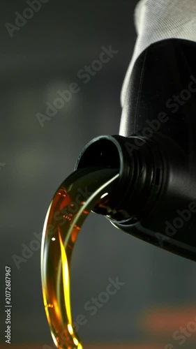 Super slow motion (1000 fps) cinematic shot of motor oil pouring from a container with dynamic camera movement around the bottle neck. Golden liquid flow with bubbles and reflections