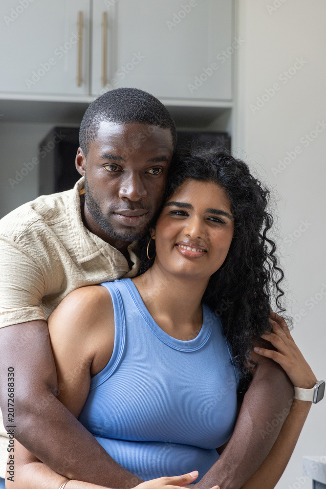 Obraz premium Diverse couple hugging in kitchen man holding Indian woman wearing blue tank, smartwatch visible
