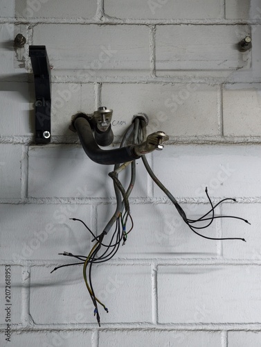 Fotografie Exposed electrical cables and hydraulic hoses emerging from white painted cinder