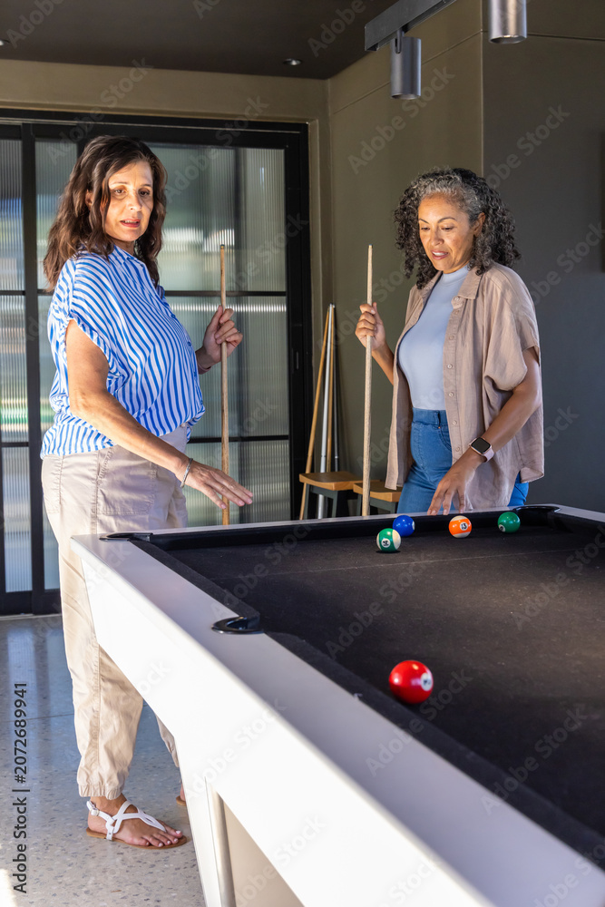 Naklejka premium Diverse female friends standing at black felt pool table, holding cues and examining ball cluster