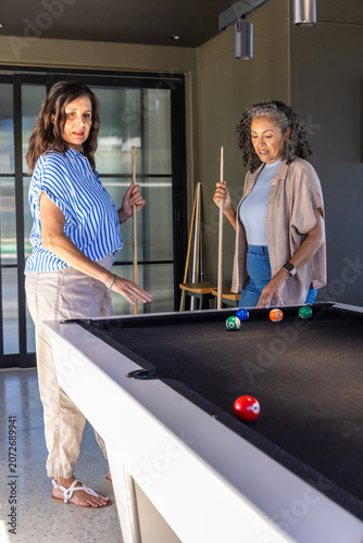 Diverse female friends standing at black felt pool table, holding cues and examining ball cluster