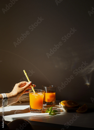 Fresh orange juice in glasses with ice cubes and mint in harsh sunlight. A high-angle studio shot of two glasses filled with vibrant orange juice or citrus smoothie. The scene is illuminated by harsh,