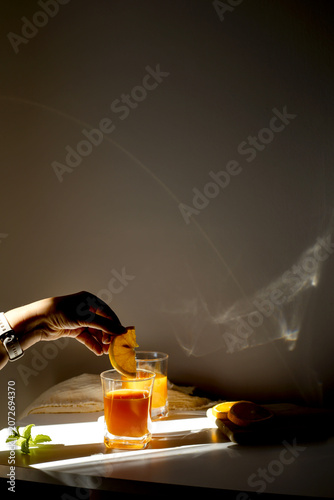 Fresh orange juice in glasses with ice cubes and mint in harsh sunlight. A high-angle studio shot of two glasses filled with vibrant orange juice or citrus smoothie. The scene is illuminated by harsh,