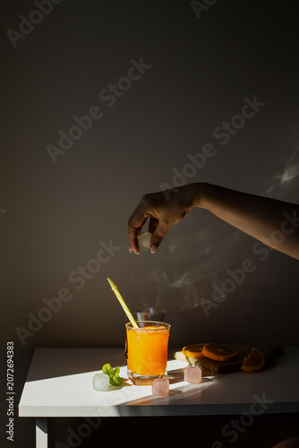 Fresh orange juice in glasses with ice cubes and mint in harsh sunlight. A high-angle studio shot of two glasses filled with vibrant orange juice or citrus smoothie. The scene is illuminated by harsh,
