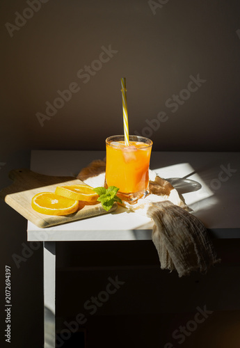 Fresh orange juice in glasses with ice cubes and mint in harsh sunlight. A high-angle studio shot of two glasses filled with vibrant orange juice or citrus smoothie. The scene is illuminated by harsh,