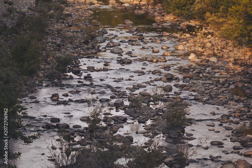 Sunlight dances on the calm river as it meanders through a rocky landscape in the serene evening glow