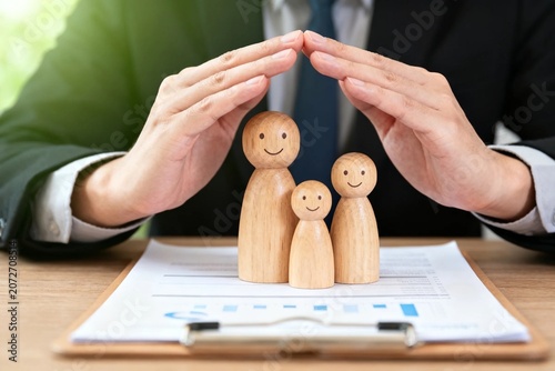 Hands Protecting Wooden Family Figures on Desk