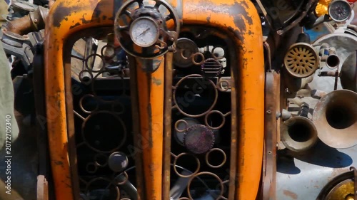 a custom steampunk-themed vehicle sculpture, front features a prominent orange grill, a circular gauge, and is detailed with numerous metallic steampunk-style gears and components