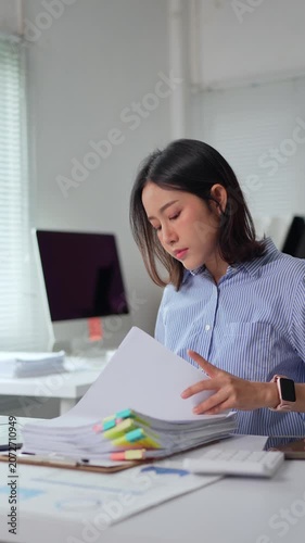 Asian businesswoman organizing documents with sticky notes at desk