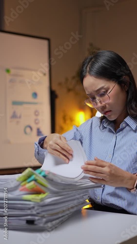 Stressed asian businesswoman searching for documents working overtime at night