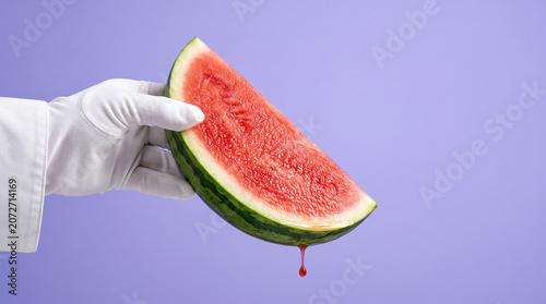 Gloved Hand Holding Juicy Watermelon Slice with Dripping Drop on Purple Background