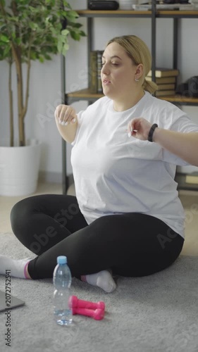 Woman sits on floor practicing fitness movements using a laptop at home.