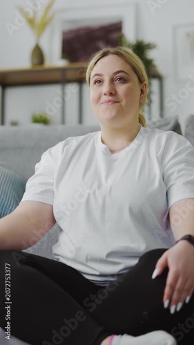 Overweight woman sits on couch at home and enjoys her time in casual clothes.