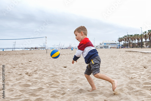 Young Boy Playing With a Colorful Beach Ball on a Sandy Shoreline During a Cloudy Afternoon
