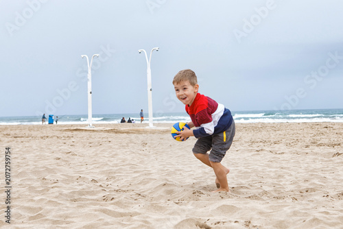 Young Boy Playing With a Colorful Beach Ball on a Sandy Shoreline During a Cloudy Afternoon
