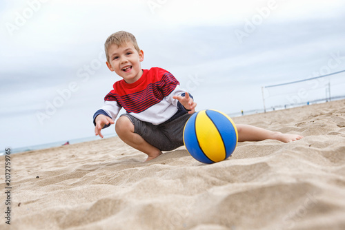 Young Boy Playing With a Colorful Beach Ball on a Sandy Shoreline During a Cloudy Afternoon