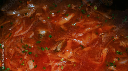 Close-up view of a rich red soup borsh with shredded vegetables and herbs