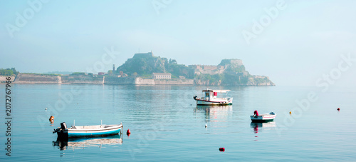 Beautiful landscape with boats in the morning fog against the background of the old fortress in Corfu, Greece