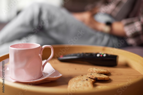 Person enjoying a quiet moment, relaxing on the couch with a cup of coffee or tea, chocolate chip cookies, and tv remote