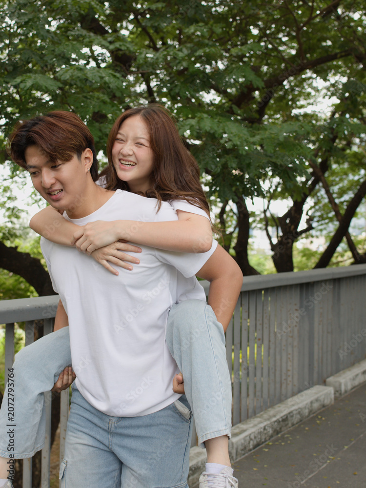 Fototapeta premium Happy Young Asian Couple Enjoying Piggyback Ride in Benchakitti Park
