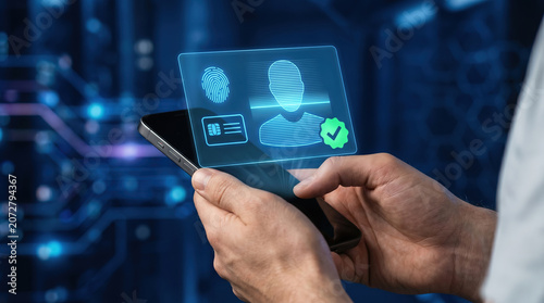 Close-up of hands holding a smartphone, floating holographic of a faceless human silhouette with horizontal scanning lines passing over it, fingerprint icon, ID card outline, and green verified badge