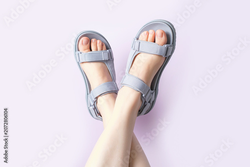 Female legs in gray sandals upside down on purple background, copy space.