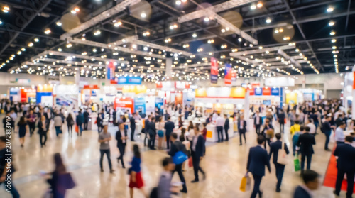 Blurred view of a crowded trade show exhibition hall with people walking between booths