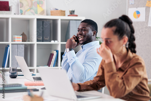 Fotografie Coworker on phone distracting stressed woman in shared office