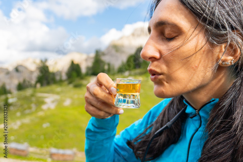 Φωτογραφία Close up woman traveler drinking local herbal spirit schnapps or grappa shot glass wooden terrace green mountain valley backdrop Dolomites Italy