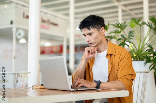 Konstfotografi Asian man focused on browsing online with laptop while sitting at table in a contemporary cafe