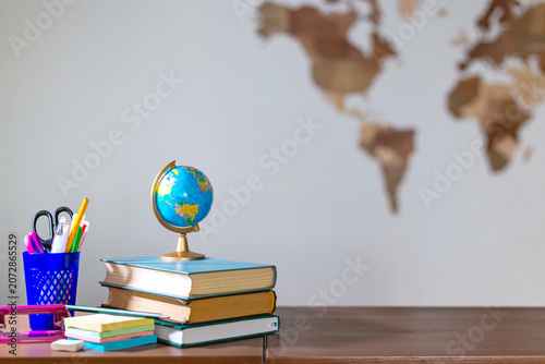 A stack of books, a globe and school stationery on a wooden tabletop.  Copy space.