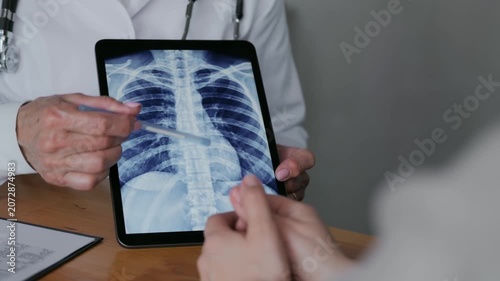 Medical professional explaining chest X-ray results to a patient using a digital tablet during a clinical consultation.