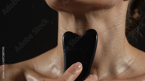 Extreme close-up of a woman massaging her neck and collarbone with a black jade gua sha stone tool for lymphatic drainage.