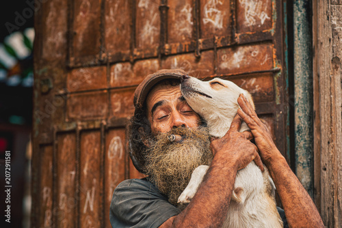 Cuadro en lienzo Bearded Cuban man holding his beloved dog while smoking a traditional cigar in Old Havana, Cuba