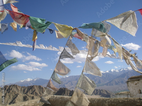 Colorful Tibetan prayer flags fluttering in the wind against a backdrop of the Himalayan mountain range in Ladakh, India.