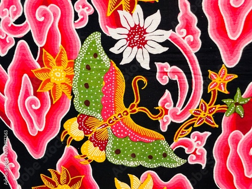 Foto A beautiful Indonesian batik fabric featuring butterfly, flower, leaf, and cloud motifs from Cirebon, dominated by red and black colors