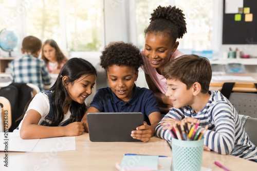 Diverse group of happy students using a digital tablet together in a modern classroom.