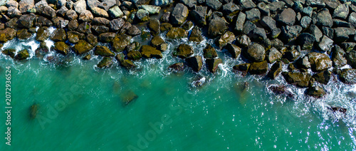 Top down aerial drone perspective of ocean water meeting the rugged stones of a breakwater