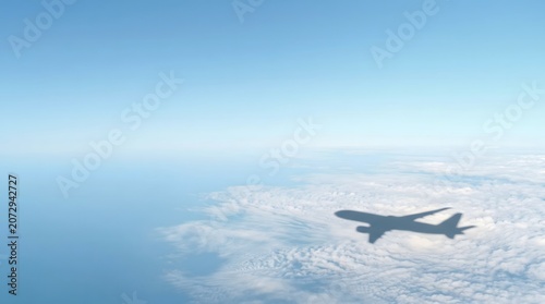 Aerial view of a commercial airplane shadow cast onto a thick white cloud layer under a clear blue sky during a sunny day flight.