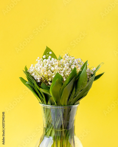 Lily of valley flowers in glass vase on yellow background, spring floral arrangement