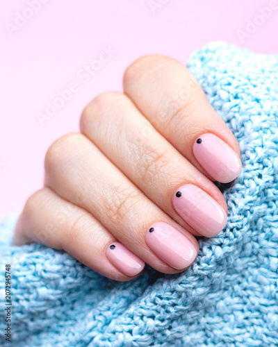 Manicured hand with minimalist nail art, pink polish and black dots on blue knitted fabric