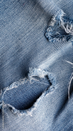 Ripped blue denim jeans texture, close up view of distressed fabric with frayed edges