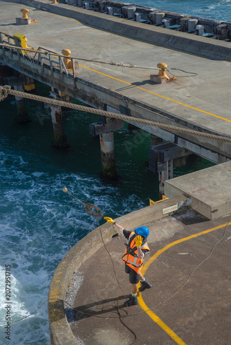 Man in the harbor of Wellington throwing a line to the ferry boat from Picton to Wellington docking in the harbor at the ferry landing.